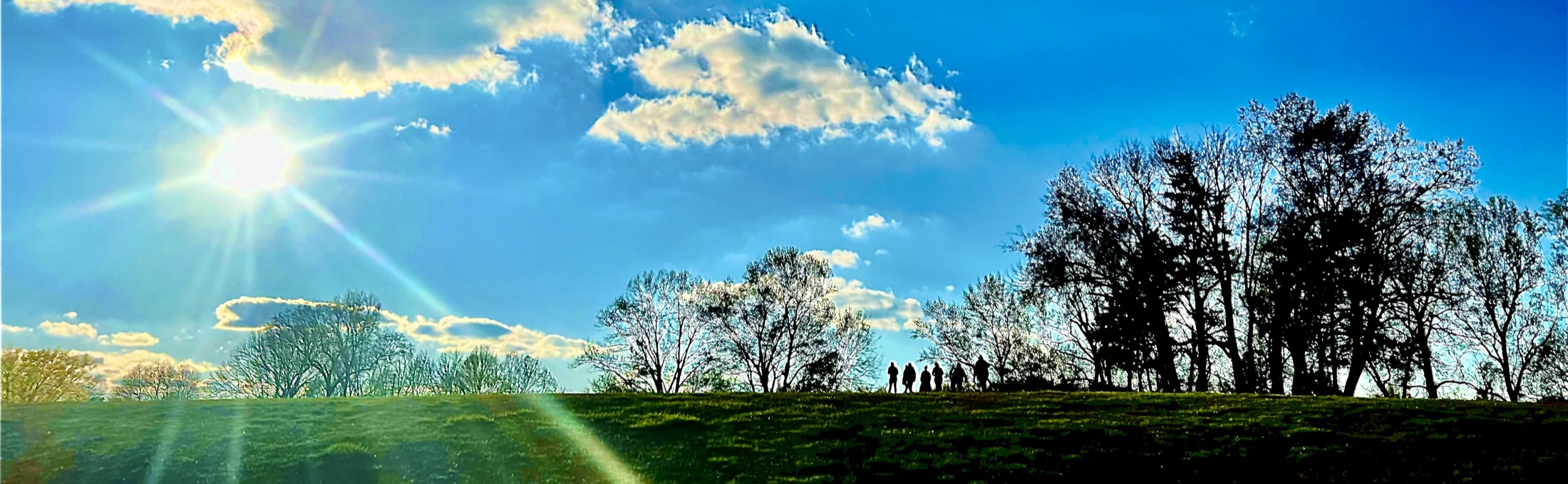 Actors gather on a hillside beneath a bright sky